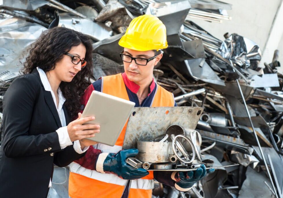 Workers discussing with tablet at scrapyard.